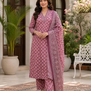 May include: A mauve-colored three-piece outfit consisting of a long-sleeved kurta with a V-neckline, matching straight-leg trousers, and a coordinating dupatta, all featuring a repeating white floral block print pattern throughout the fabric.