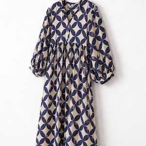 May include: A midi-length dress featuring a beige base with a repeating dark navy blue circular geometric pattern. The dress has long, loose sleeves with gathered cuffs, a gathered waistline, and a simple collarless neckline with a front button placket.