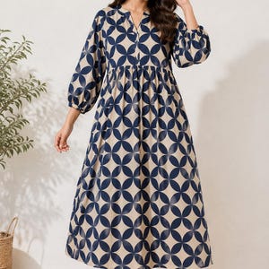 May include: A midi-length dress featuring a beige base with a repeating dark blue geometric circle pattern. The dress has a split V-neckline, long sleeves with gathered cuffs, and a gathered waistline that flows into a loose, full skirt.