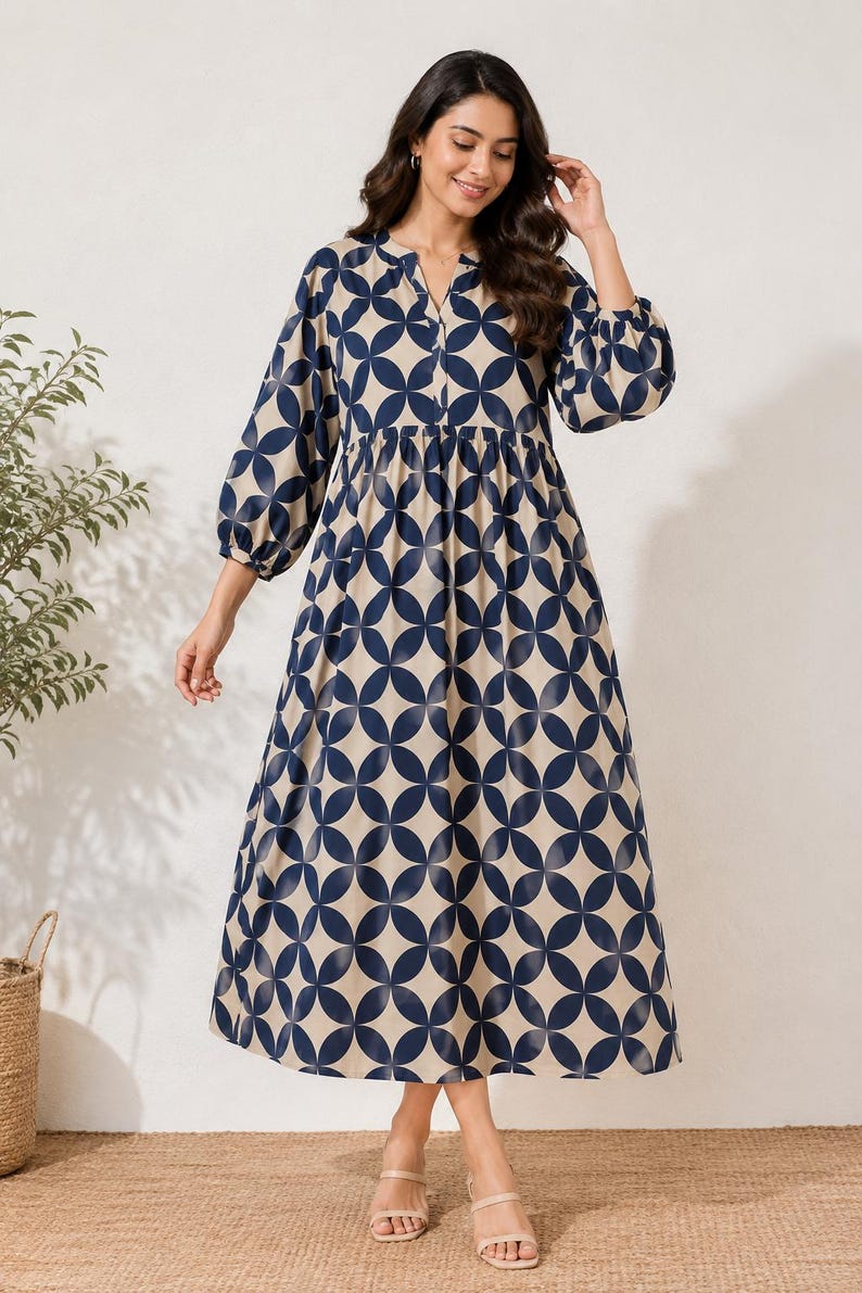 May include: A midi-length dress featuring a beige base with a repeating dark blue geometric circle pattern. The dress has a split V-neckline, long sleeves with gathered cuffs, and a gathered waistline that flows into a loose, full skirt.