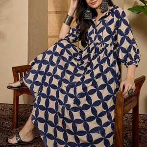 May include: A long-sleeved maxi dress featuring a repeating navy blue geometric circle pattern on a beige background. The dress has a collared neckline, a gathered waistline, and voluminous sleeves that extend to the elbows, creating a flowing silhouette.