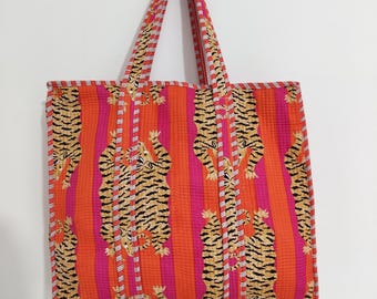 Könnte beinhalten: Eine gesteppte Tragetasche mit einem lebendigen Design. Die Tasche hat ein Muster aus orangefarbenen und rosa vertikalen Streifen, durchsetzt mit Tigerdruckmotiven. Die Griffe und der Besatz haben einen passenden Tigerdruck. Die Tasche hängt an einer Wand.