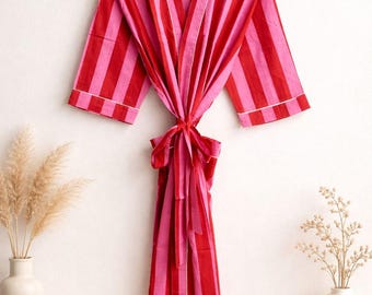 May include: A red and pink striped robe with white trim, hanging on a wooden hanger. The robe is tied at the waist with a matching belt. The sleeves are short, and the fabric appears lightweight.