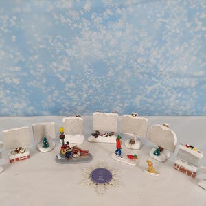 Könnte beinhalten: Eine Sammlung von Miniatur-Weihnachtsdorf-Figuren, darunter schneebedeckte Schilder, ein Gitarrist, eine Person, die einen Hund ausführt, und ein Weihnachtsbaum. Die Figuren sind vor einem verschneiten blauen Hintergrund platziert.