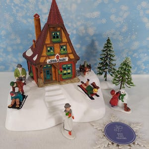 Pode incluir: Uma cena de aldeia de inverno em miniatura com uma casa alta de estrutura de madeira com telhado vermelho e uma placa com a inscrição Franz Schiller Kuckuck Uhren. O conjunto inclui várias figuras pequenas em trenós, uma pessoa de pé, um boneco de neve e dois pinheiros.