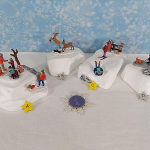 May include: Four white miniature snowy platforms featuring winter scenes: A shows people and a dog, B features two deer, C displays a skier and a person on a sled, and D depicts people on a bench with a dog. Each platform is labeled with a star.