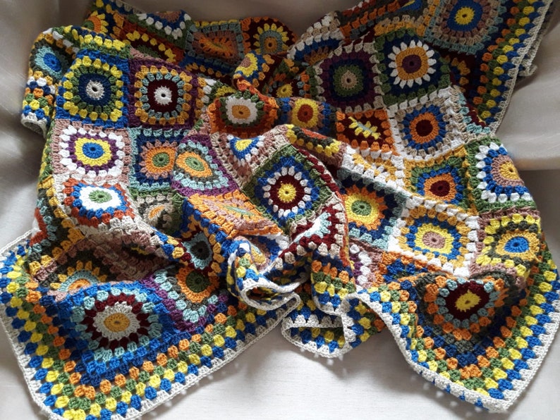 May include: A colorful crocheted blanket with a variety of squares in shades of blue, green, yellow, orange, red, and brown. The blanket is made with a granny square pattern and has a white border.
