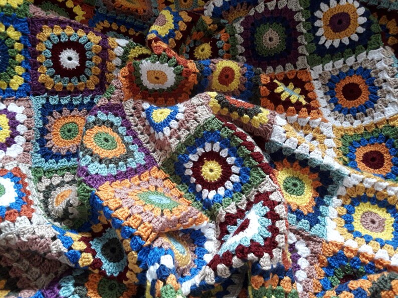 May include: A colorful crocheted blanket with a variety of square patterns in shades of brown, blue, green, yellow, orange, red, and white.