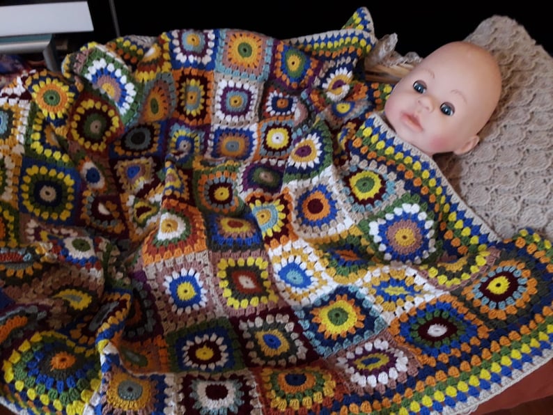 May include: A colorful crocheted baby blanket with a variety of colors and patterns, including squares and circles. The blanket is made with a variety of yarn colors, including brown, white, yellow, green, blue, and red.