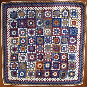 May include: A crocheted blanket with a square pattern in shades of blue, red, white, and yellow. The blanket is made up of individual squares that are joined together to create a larger design.
