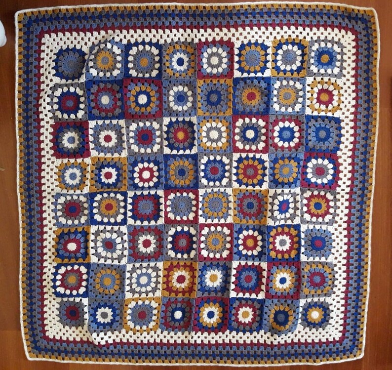 May include: A crocheted blanket with a square pattern in shades of blue, red, white, and yellow. The blanket is made up of individual squares that are joined together to create a larger design.