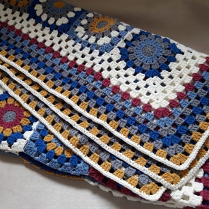 May include: A crocheted throw blanket with a multi-colored granny square pattern in shades of blue, gray, white, red, and gold.