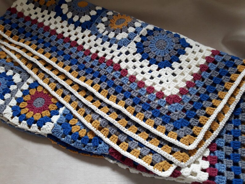 May include: A crocheted throw blanket with a multi-colored granny square pattern in shades of blue, gray, white, red, and gold.