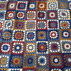 May include: A crocheted blanket with a patchwork design featuring squares in shades of blue, red, white, and gold.