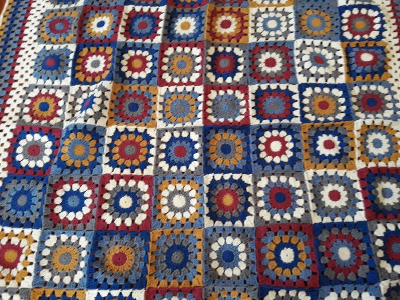 May include: A crocheted blanket with a patchwork design featuring squares in shades of blue, red, white, and gold.