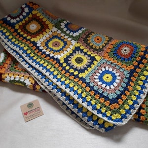 May include: A colorful crocheted blanket with a granny square pattern in shades of blue, green, yellow, orange, and brown. The blanket has a white border.