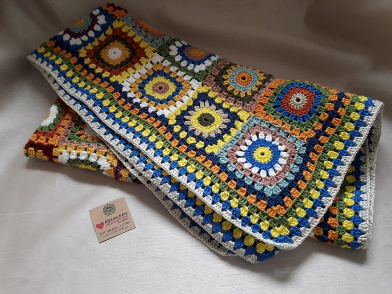 May include: A colorful crocheted blanket with a granny square pattern in shades of blue, green, yellow, orange, and brown. The blanket has a white border.