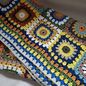 May include: A colorful crocheted blanket with a geometric pattern of squares and circles in shades of orange, yellow, green, blue, and brown.