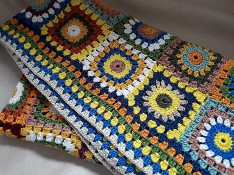May include: A colorful crocheted blanket with a geometric pattern of squares and circles in shades of orange, yellow, green, blue, and brown.