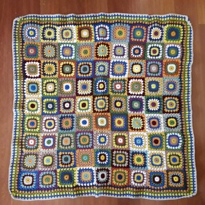 May include: A colorful crocheted blanket with a square pattern. The blanket is made with different shades of blue, green, yellow, red, and brown yarn.