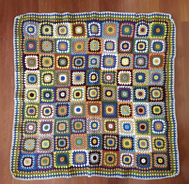 May include: A colorful crocheted blanket with a square pattern. The blanket is made with different shades of blue, green, yellow, red, and brown yarn.