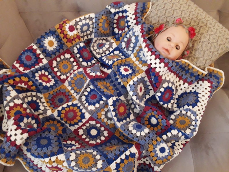 May include: A crocheted blanket with a colorful granny square pattern in shades of blue, red, white, and yellow. The blanket is made of soft yarn and has a delicate texture.