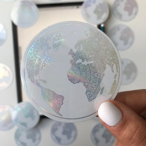 May include: A white, iridescent sticker with a detailed outline of the Earth. The sticker has a mandala-like design.