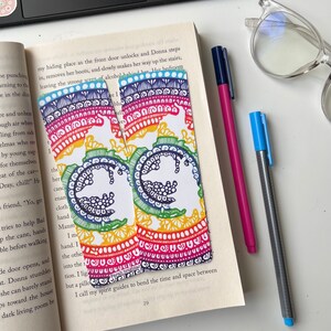 Könnte beinhalten: Zwei regenbogenfarbene Lesezeichen mit komplizierten Mandala-Designs. Die Lesezeichen haben einen weißen Hintergrund mit einer schwarzen und weißen Silhouette eines Vogels in der Mitte. Der Text "Farah Bright" ist auf der Unterseite eines Lesezeichens sichtbar.