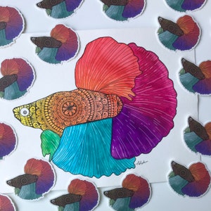 May include: A colorful, hand-painted betta fish with intricate mandala patterns on its body. The fish is depicted in a vibrant palette of red, orange, yellow, blue, purple, and green. The artwork is framed by a white border.