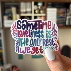May include: A colorful sticker with the text "Sometimes loneliness is the only rest we get" surrounded by floral designs.