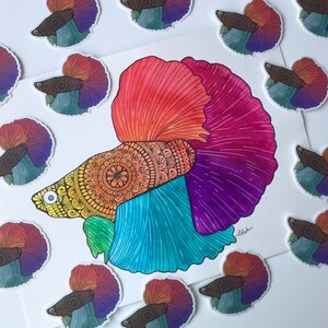 May include: A colorful watercolor painting of a betta fish with intricate mandala patterns on its body. The fish is depicted with a red, pink, purple, blue, and yellow color scheme. The painting is surrounded by smaller images of betta fish in various colors.
