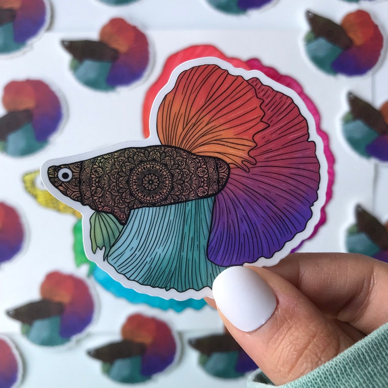 May include: A colorful sticker of a betta fish with a mandala pattern on its body. The fish is outlined in black and has a rainbow-colored tail fin.