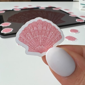 May include: A pink seashell sticker with a detailed, intricate design. The sticker is on a white background.