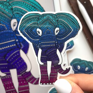 May include: A sticker of an elephant with a blue and purple mandala design. The elephant is standing with its trunk raised.