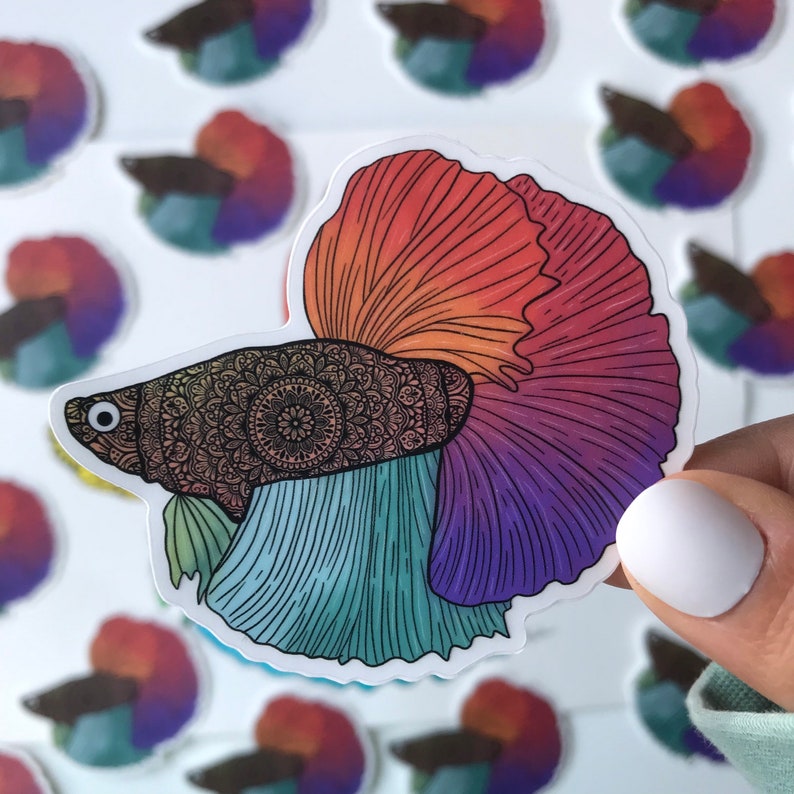 May include: A colorful sticker of a betta fish with a mandala pattern on its body. The fish has a red, orange, purple, and blue tail fin.
