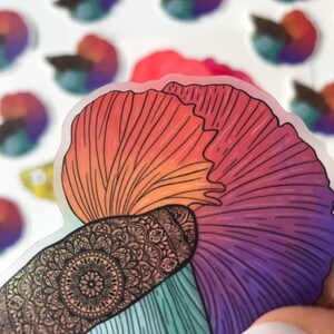 May include: A colorful sticker of a betta fish with a mandala design on its body. The fish is depicted with a long, flowing tail and fins in shades of red, orange, purple, and blue.