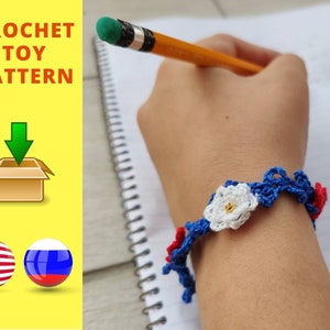 May include: A crochet bracelet with a white flower design and red, white, and blue accents. The bracelet is on a person's wrist. The image also includes the text "CROCHET TOY PATTERN" and a download arrow.