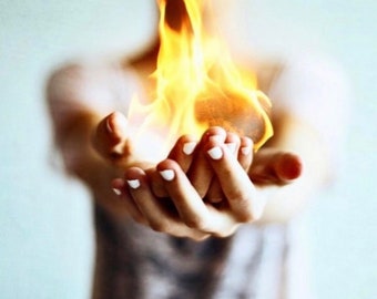 May include: A person's hands cupped around a bright orange flame. The flame is burning brightly and the person's hands are slightly blurred.