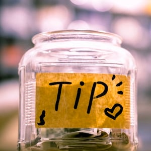 May include: A clear glass jar with a brown paper label that says "Tip" in black marker. There is a small heart drawn on the label.
