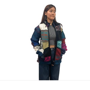 Peut inclure: Une veste en patchwork multicolore avec une fermeture éclair. La veste est faite de différents tissus tricotés dans des tons de bleu, vert, rouge, rose et blanc.