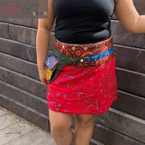 Puede incluir: Minifalda roja con estampado floral y ri&ntilde;onera multicolor. El cintur&oacute;n tiene un dise&ntilde;o marr&oacute;n, naranja y azul. La persona lleva un top negro y zapatillas blancas.