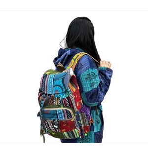 May include: A vibrant patchwork backpack featuring a mix of patterns and colours, such as blue, red, green, and yellow. The backpack has a front pocket and adjustable straps. The person is wearing a blue patchwork jacket.