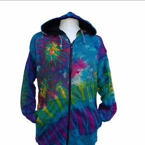 Può includere: Una felpa con cappuccio con zip tie-dye con cappuccio nero. La felpa presenta un motivo tie-dye colorato in tonalità di blu, verde, viola, giallo e rosa.