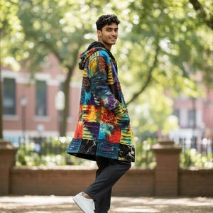 May include: A long, patchwork coat with a hood, featuring a vibrant mix of colors including red, yellow, blue, and purple. The coat is worn with dark gray pants and white sneakers. The background shows a park setting with trees and a brick wall.