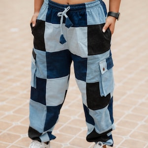 May include: Cargo pants featuring a checkered pattern in alternating shades of light blue, medium blue, and black. The pants have an elastic waistband with a drawstring, two side pockets, and two large cargo pockets on the thighs with button flaps.