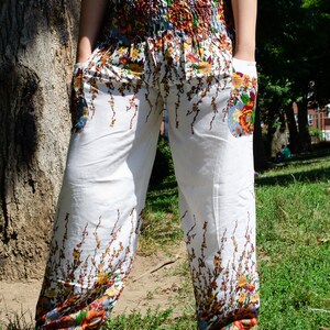 May include: White pants with a floral print featuring brown, orange, and yellow flowers. The pants have a wide leg and a drawstring waist.