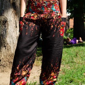 May include: Black pants with a floral print in shades of red, yellow, blue, and green. The pants have a wide leg and a drawstring waist.