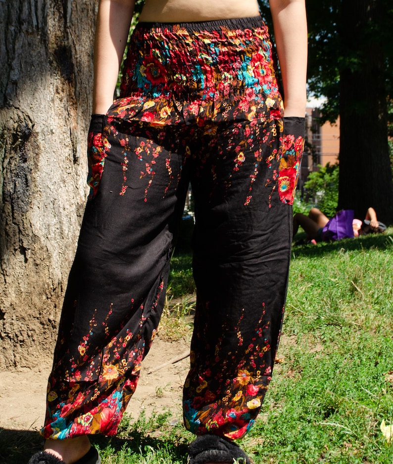 May include: Black pants with a floral print in shades of red, yellow, blue, and green. The pants have a wide leg and a drawstring waist.