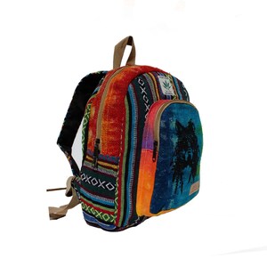 May include: Multicolored woven backpack with a blue pocket featuring a black wolf silhouette. The backpack has a brown leather strap and a green leaf logo.