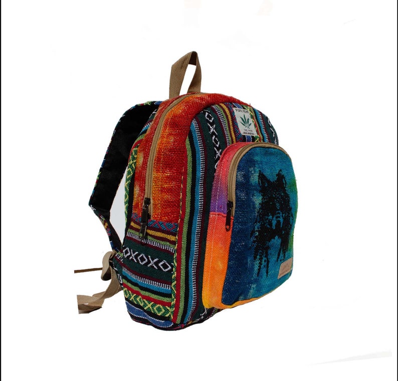 May include: Multicolored woven backpack with a blue pocket featuring a black wolf silhouette. The backpack has a brown leather strap and a green leaf logo.